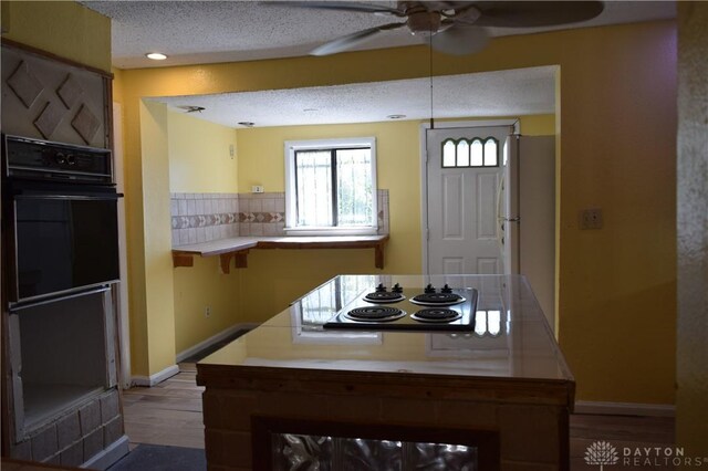 kitchen featuring kitchen peninsula, oven, a textured ceiling, stainless steel stovetop, and light wood-type flooring