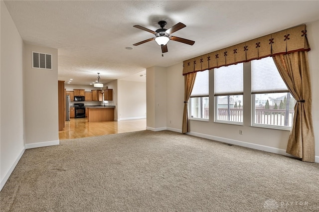 unfurnished living room featuring light carpet, a textured ceiling, and ceiling fan