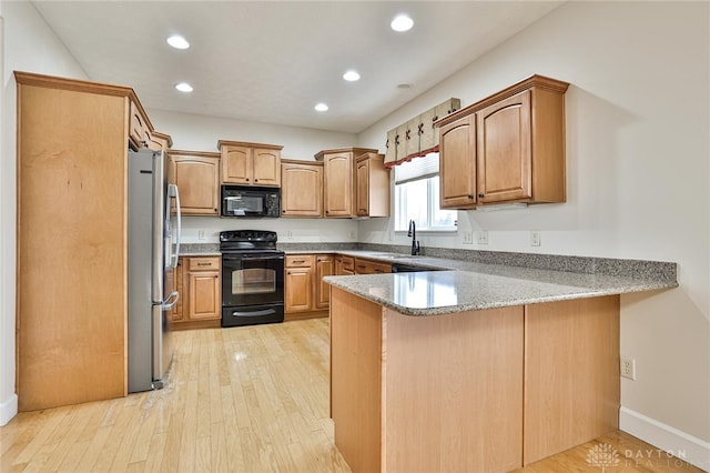 kitchen with stone countertops, black appliances, sink, light hardwood / wood-style floors, and kitchen peninsula