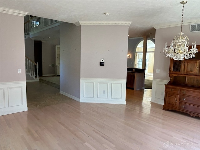 empty room featuring light hardwood / wood-style floors, crown molding, a notable chandelier, and a textured ceiling