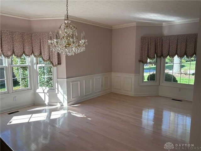 unfurnished dining area with ornamental molding, an inviting chandelier, light hardwood / wood-style floors, and a wealth of natural light