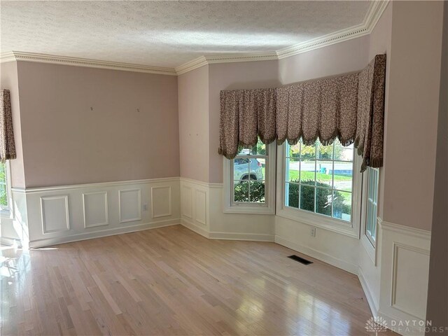 spare room with a textured ceiling, light wood-type flooring, and crown molding