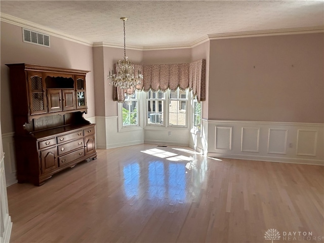 unfurnished dining area with light hardwood / wood-style floors, ornamental molding, and a textured ceiling