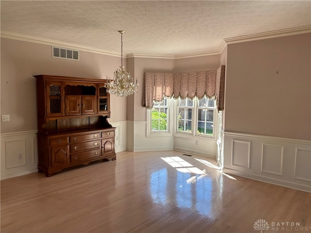 unfurnished dining area featuring an inviting chandelier, a textured ceiling, light hardwood / wood-style flooring, and ornamental molding