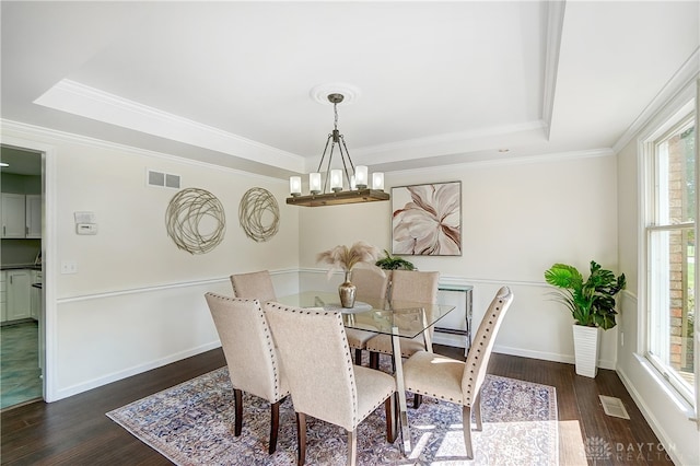 dining room featuring dark wood-type flooring, ornamental molding, a tray ceiling, and an inviting chandelier