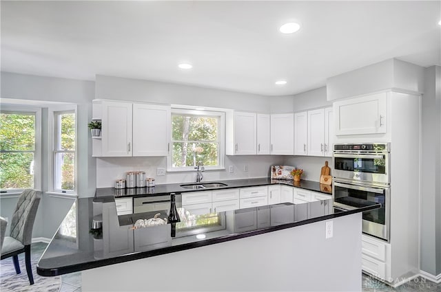 kitchen featuring white cabinetry, double oven, sink, and kitchen peninsula