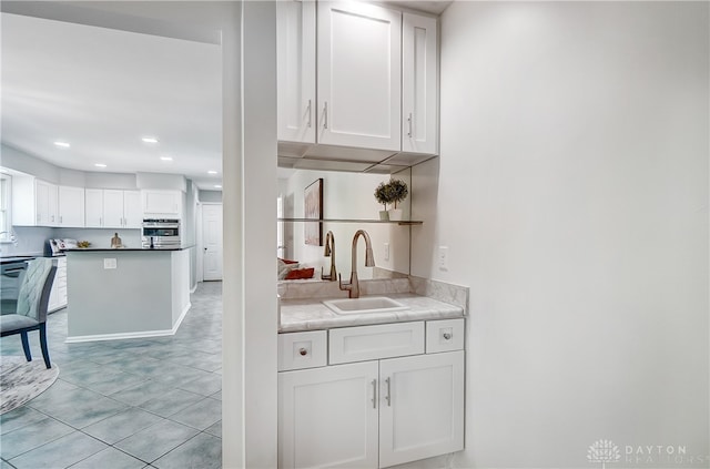 bar with sink, white cabinetry, stainless steel oven, and light tile patterned floors