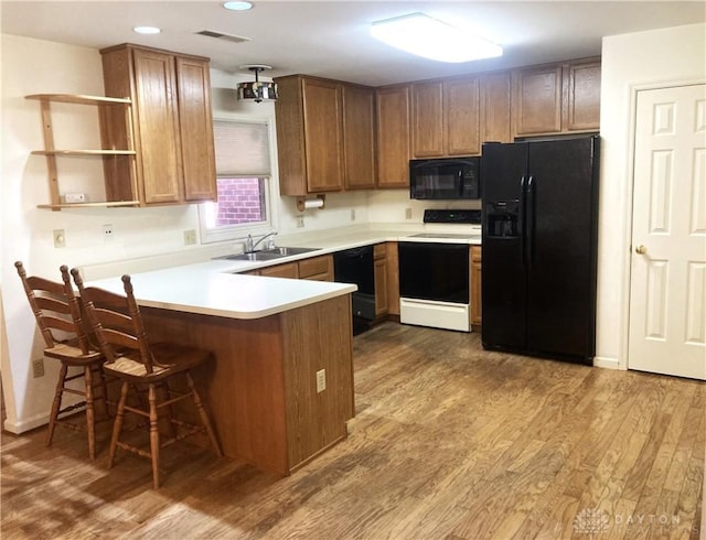 kitchen with a breakfast bar, black appliances, sink, kitchen peninsula, and light wood-type flooring