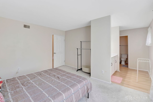 bedroom with light wood-type flooring and ensuite bath