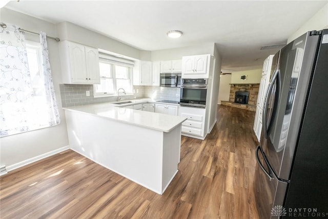 kitchen with kitchen peninsula, appliances with stainless steel finishes, backsplash, sink, and white cabinets