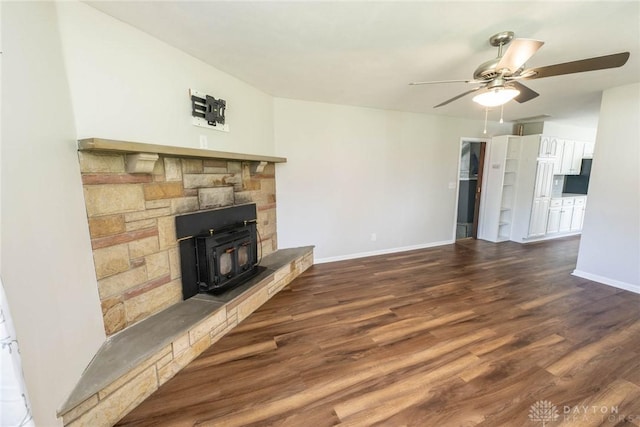 unfurnished living room featuring a wood stove, ceiling fan, and dark hardwood / wood-style floors