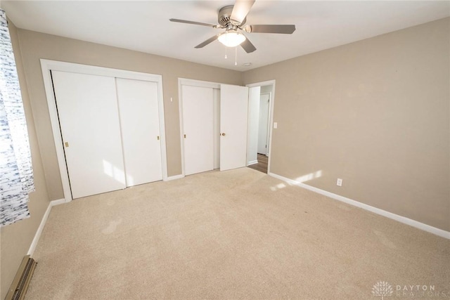 unfurnished bedroom featuring carpet flooring, ceiling fan, and multiple closets