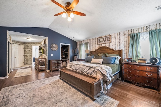 bedroom with lofted ceiling, wood-type flooring, a textured ceiling, and ceiling fan