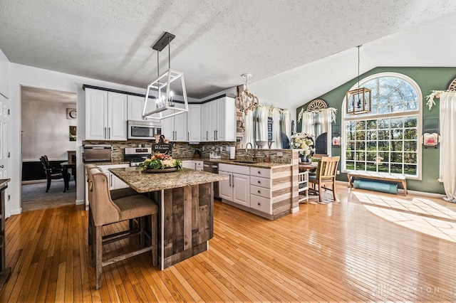 kitchen featuring lofted ceiling, sink, light hardwood / wood-style flooring, white cabinetry, and appliances with stainless steel finishes