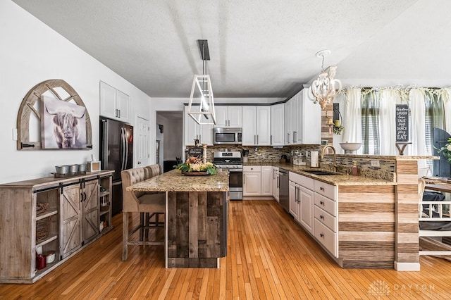 kitchen with stainless steel appliances, a breakfast bar, sink, light hardwood / wood-style flooring, and decorative light fixtures