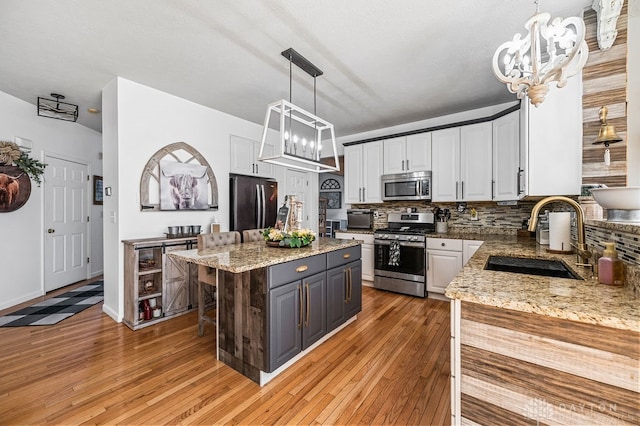 kitchen with a center island, stainless steel appliances, sink, hanging light fixtures, and white cabinetry