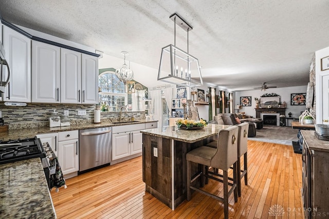 kitchen with a textured ceiling, appliances with stainless steel finishes, white cabinetry, and light hardwood / wood-style flooring