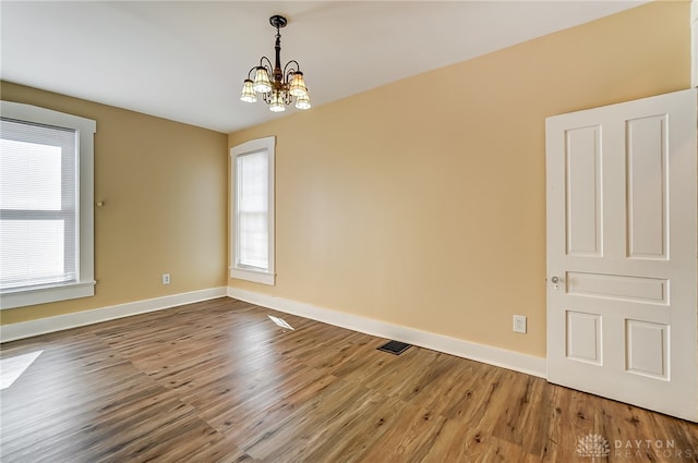 unfurnished room featuring hardwood / wood-style flooring, plenty of natural light, and a notable chandelier