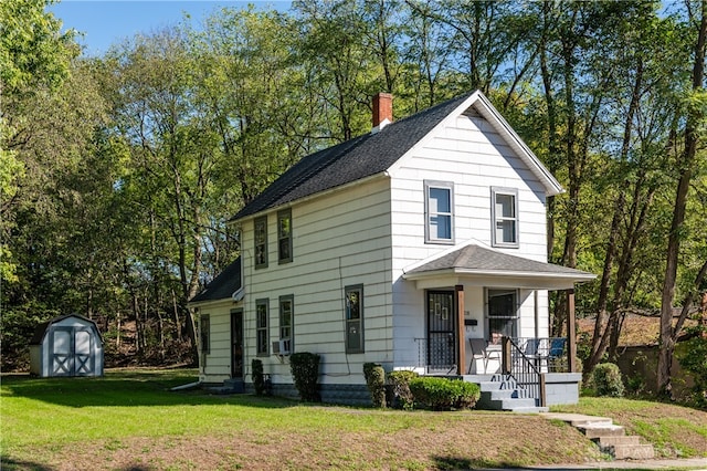 view of front of house featuring an outbuilding, a porch, a shingled roof, a front lawn, and a storage shed