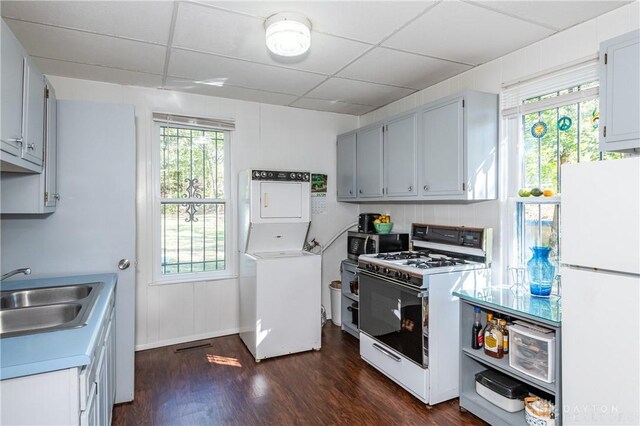 kitchen with a paneled ceiling, dark wood-type flooring, white appliances, sink, and stacked washing maching and dryer