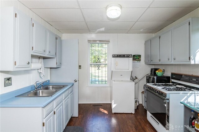 kitchen featuring dark hardwood / wood-style floors, stacked washing maching and dryer, sink, and gas range gas stove