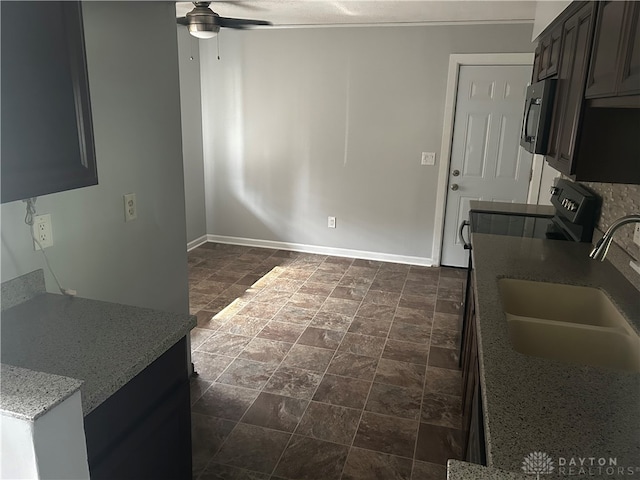 kitchen with ceiling fan, stove, light stone countertops, and sink