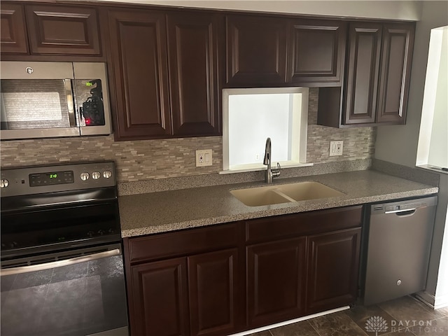 kitchen with dark brown cabinetry, sink, dark tile patterned floors, backsplash, and stainless steel appliances