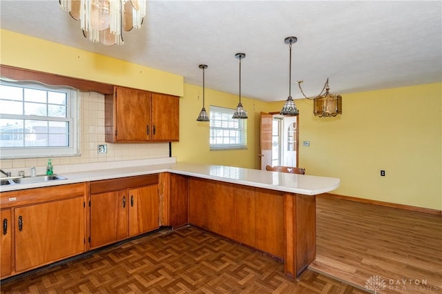 kitchen with sink, dark parquet floors, an inviting chandelier, and kitchen peninsula