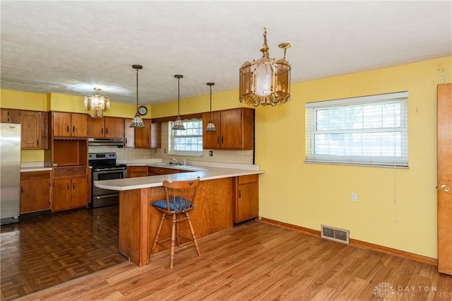 kitchen featuring stainless steel appliances, decorative light fixtures, hardwood / wood-style floors, kitchen peninsula, and decorative backsplash