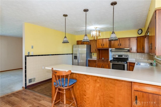 kitchen featuring kitchen peninsula, hanging light fixtures, dark hardwood / wood-style flooring, appliances with stainless steel finishes, and sink