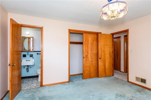 unfurnished bedroom with sink, tile walls, a closet, ensuite bath, and light colored carpet