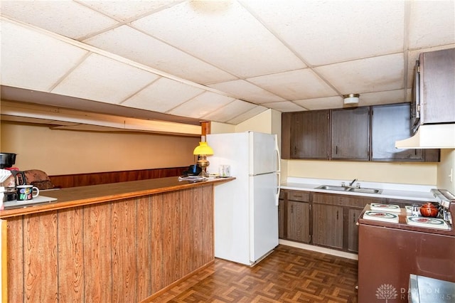 kitchen with white fridge, wood walls, a paneled ceiling, dark parquet floors, and sink