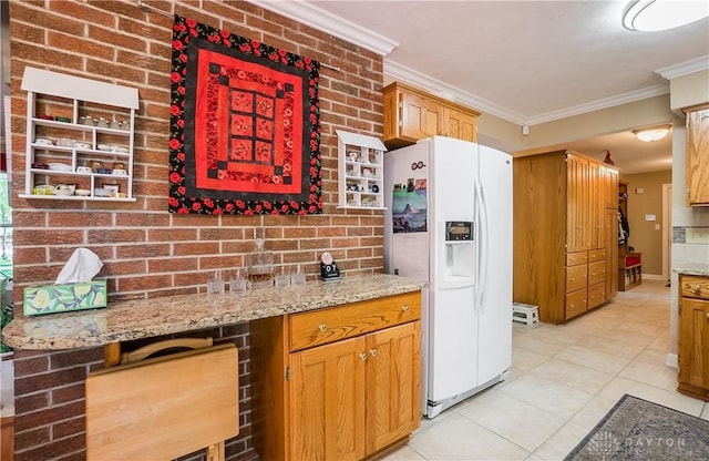 kitchen with light tile patterned flooring, brick wall, white refrigerator with ice dispenser, light stone counters, and crown molding