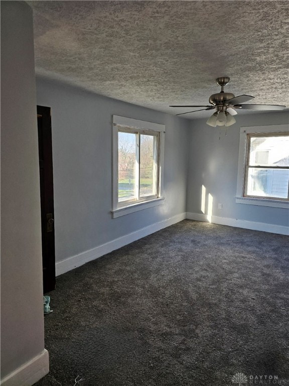 unfurnished room featuring ceiling fan, dark colored carpet, a wealth of natural light, and a textured ceiling