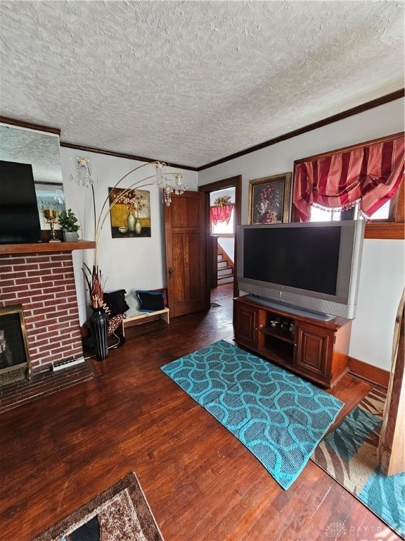 living room featuring dark wood-type flooring, a brick fireplace, ornamental molding, and a textured ceiling