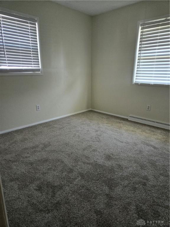 empty room with a baseboard heating unit, carpet floors, and baseboards