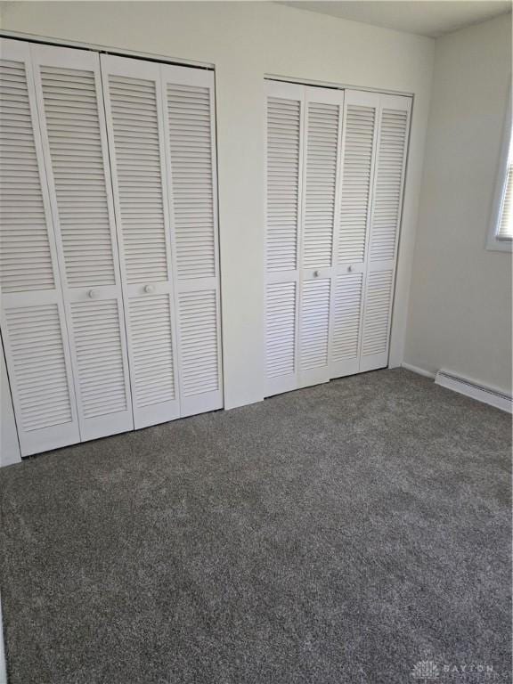 unfurnished bedroom featuring a baseboard heating unit, dark colored carpet, and two closets