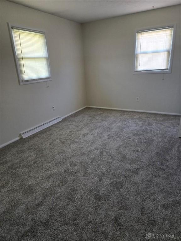 spare room featuring baseboards, baseboard heating, and dark colored carpet