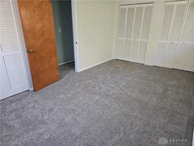 unfurnished bedroom with dark carpet and two closets