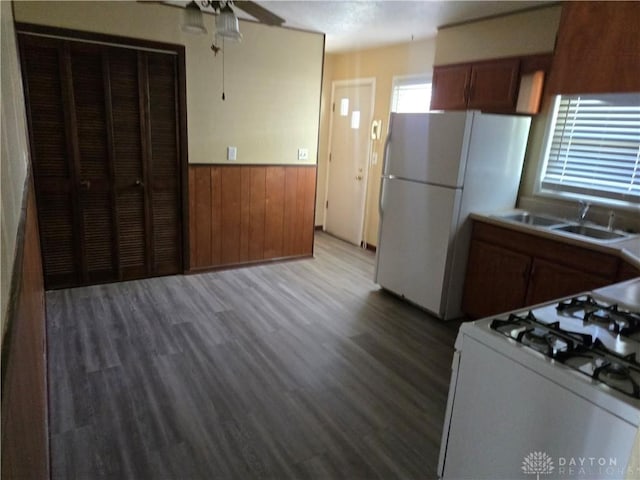 kitchen with white appliances, wood finished floors, a sink, wainscoting, and brown cabinetry