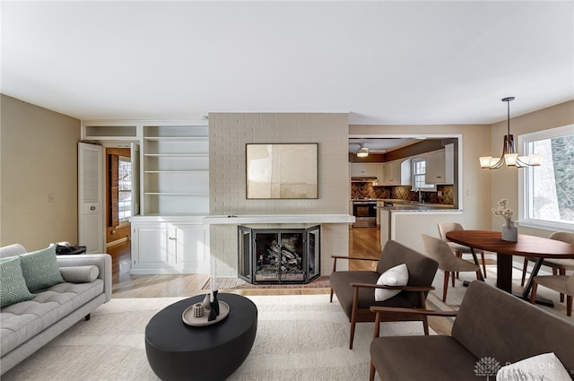 living room with sink, light wood-type flooring, an inviting chandelier, and a fireplace