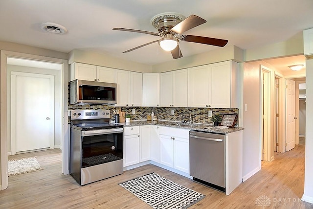 kitchen featuring white cabinets, decorative backsplash, light wood-type flooring, and stainless steel appliances