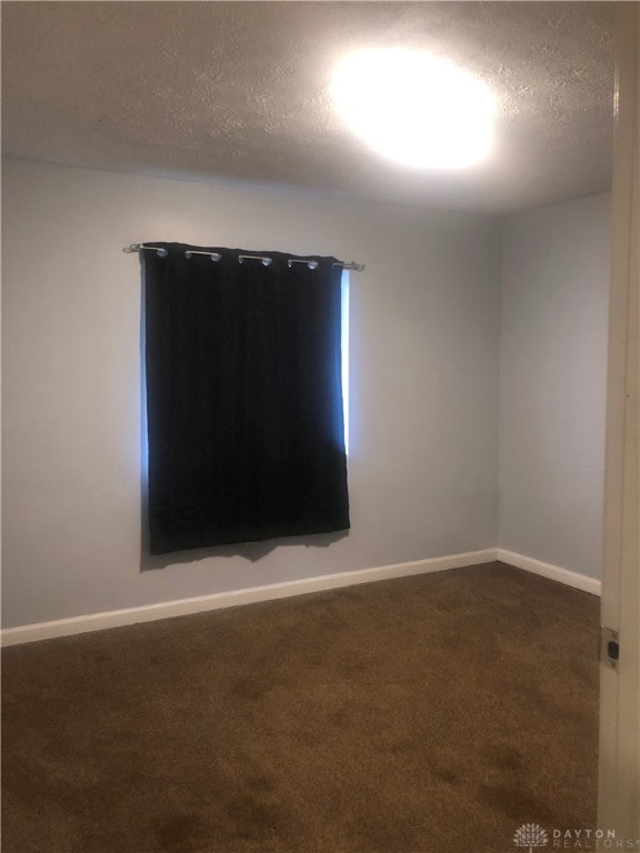 unfurnished room with dark carpet and a textured ceiling