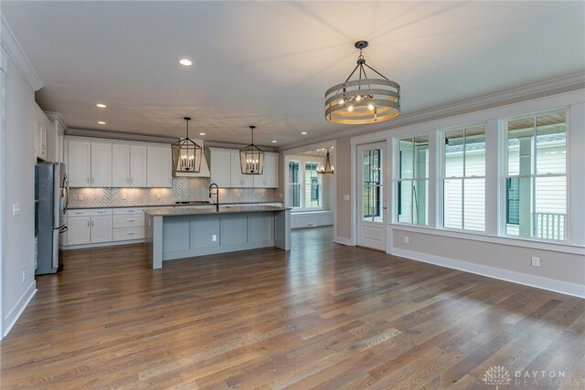 kitchen with decorative light fixtures, a center island with sink, stainless steel fridge, and ornamental molding