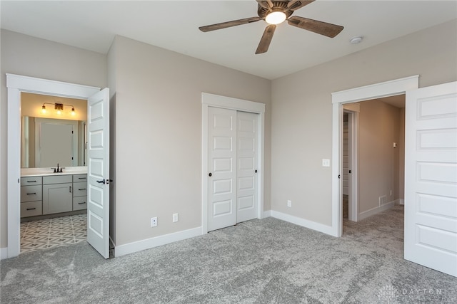 unfurnished bedroom featuring ceiling fan, connected bathroom, sink, a closet, and light colored carpet