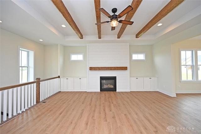 unfurnished living room with beam ceiling, light wood-type flooring, and plenty of natural light