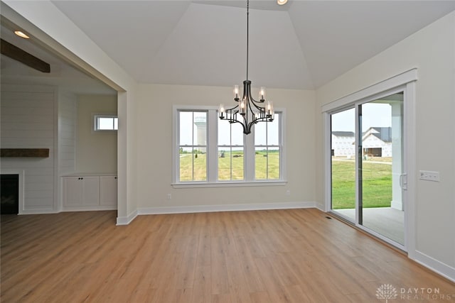 unfurnished dining area featuring an inviting chandelier, light hardwood / wood-style flooring, vaulted ceiling, and a large fireplace