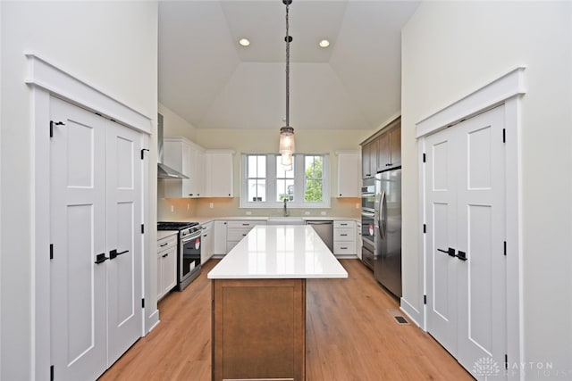 kitchen featuring light wood-type flooring, a center island, stainless steel appliances, white cabinets, and decorative light fixtures