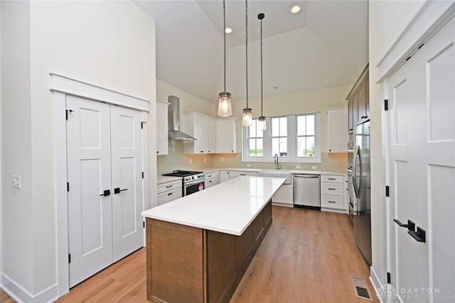 kitchen featuring wall chimney exhaust hood, a kitchen island, decorative light fixtures, white cabinets, and appliances with stainless steel finishes