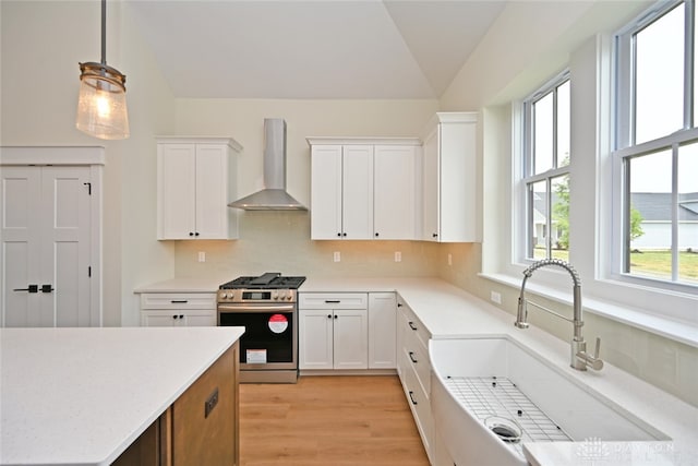 kitchen with white cabinets, wall chimney exhaust hood, decorative light fixtures, and stainless steel range with gas stovetop